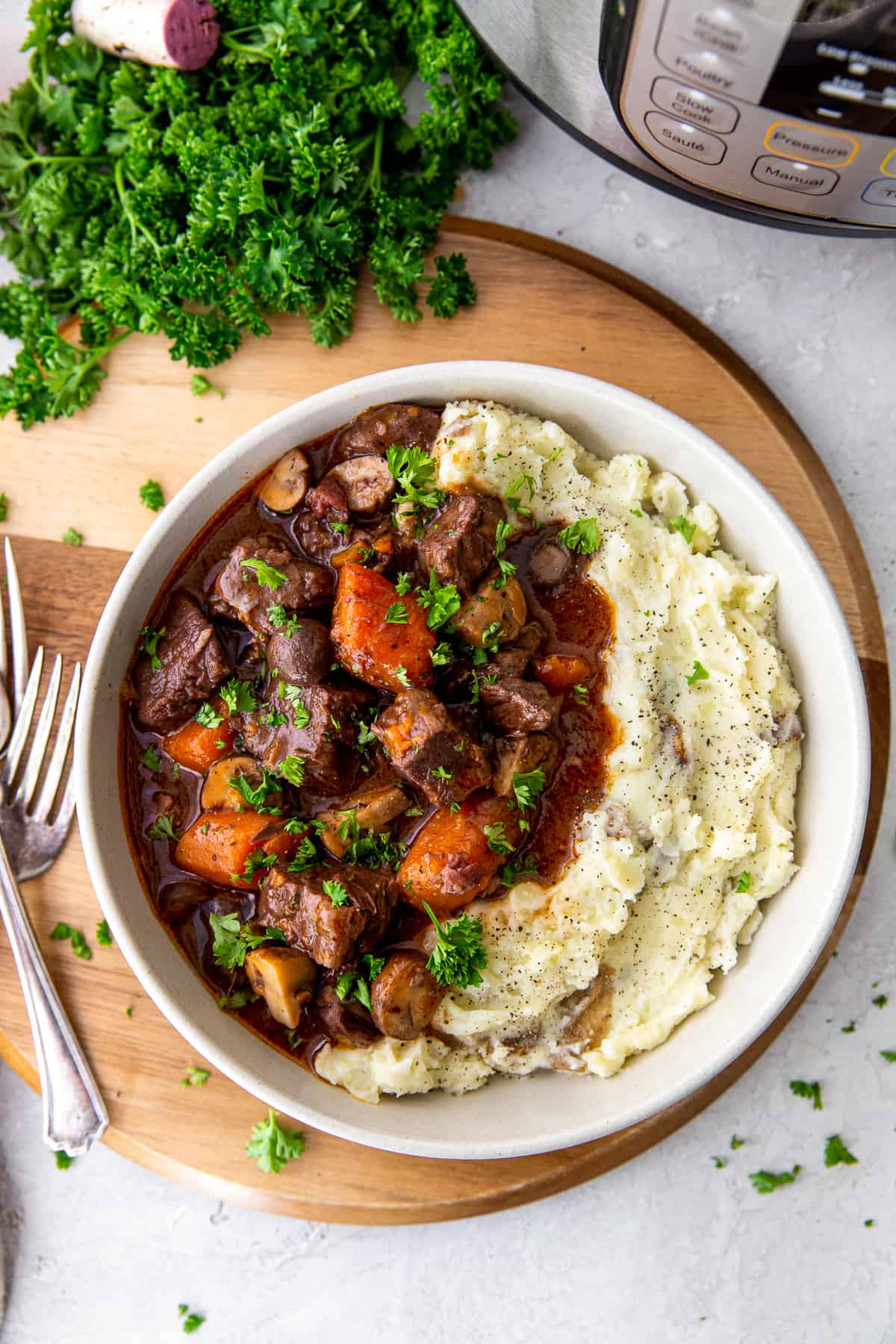 A top down view of a white bowl filled with beef burgundy and mashed potatoes with an Instant Pot behind it.