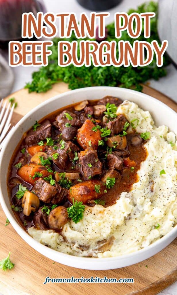 Beef burgundy with carrots and mushrooms in a white bowl with mashed potatoes in front of a glass of wine with text.