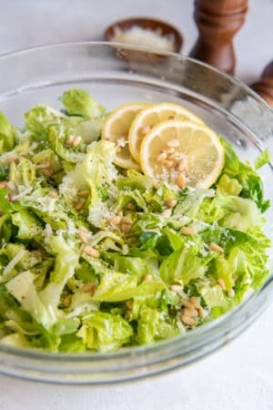 A salad of chopped romaine with Parmesan cheese and pine nuts garnished with lemon slices.