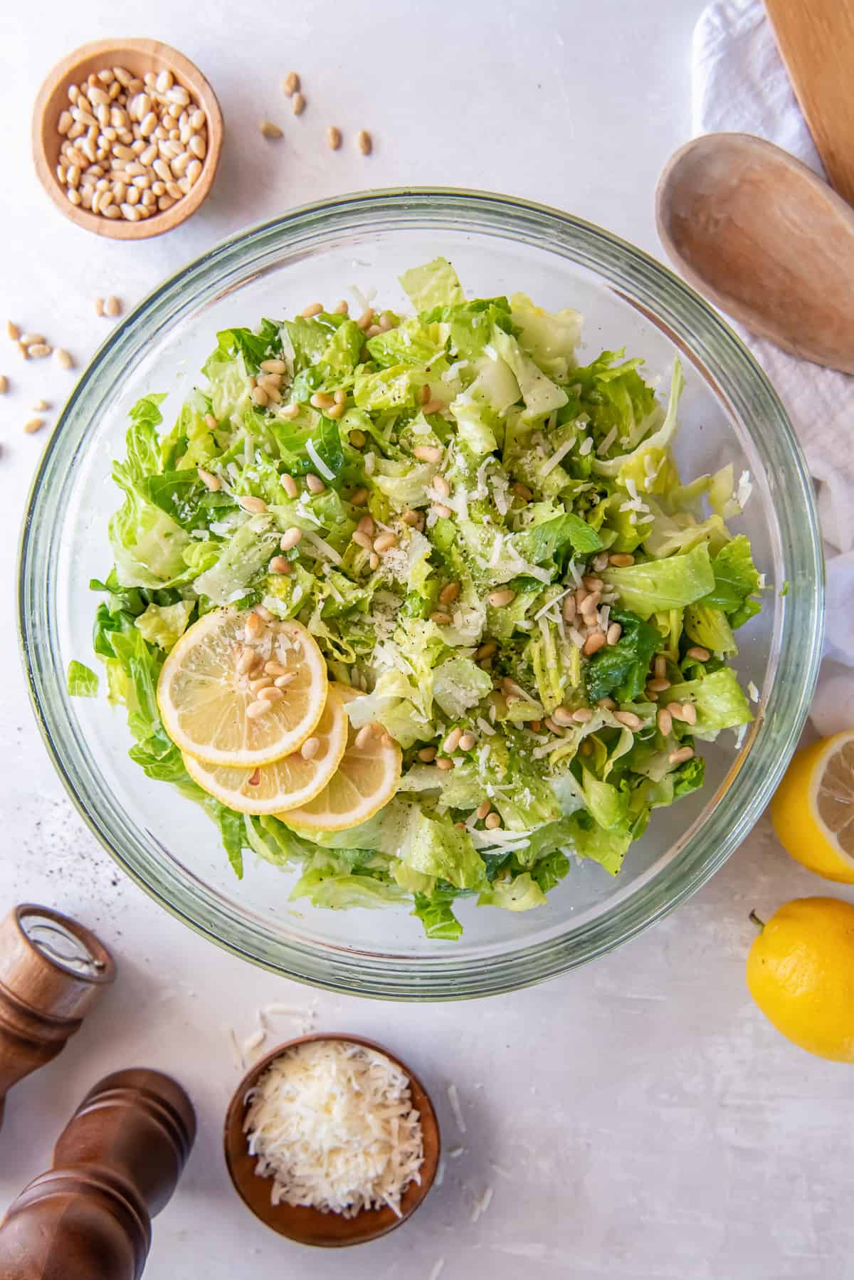 A top down shot of a salad of chopped romaine with Parmesan cheese and pine nuts garnished with lemon slices.