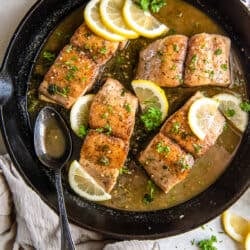 A top down shot of mahi mahi with sauce and lemon in a cast iron skillet with a metal spoon.