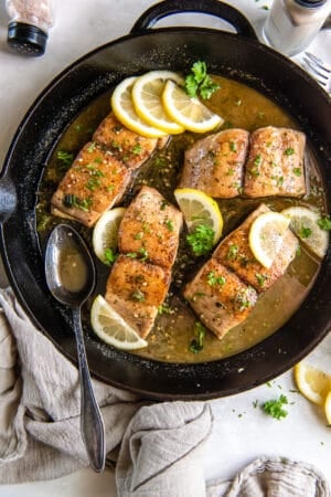 A top down shot of mahi mahi with sauce and lemon in a cast iron skillet with a metal spoon.