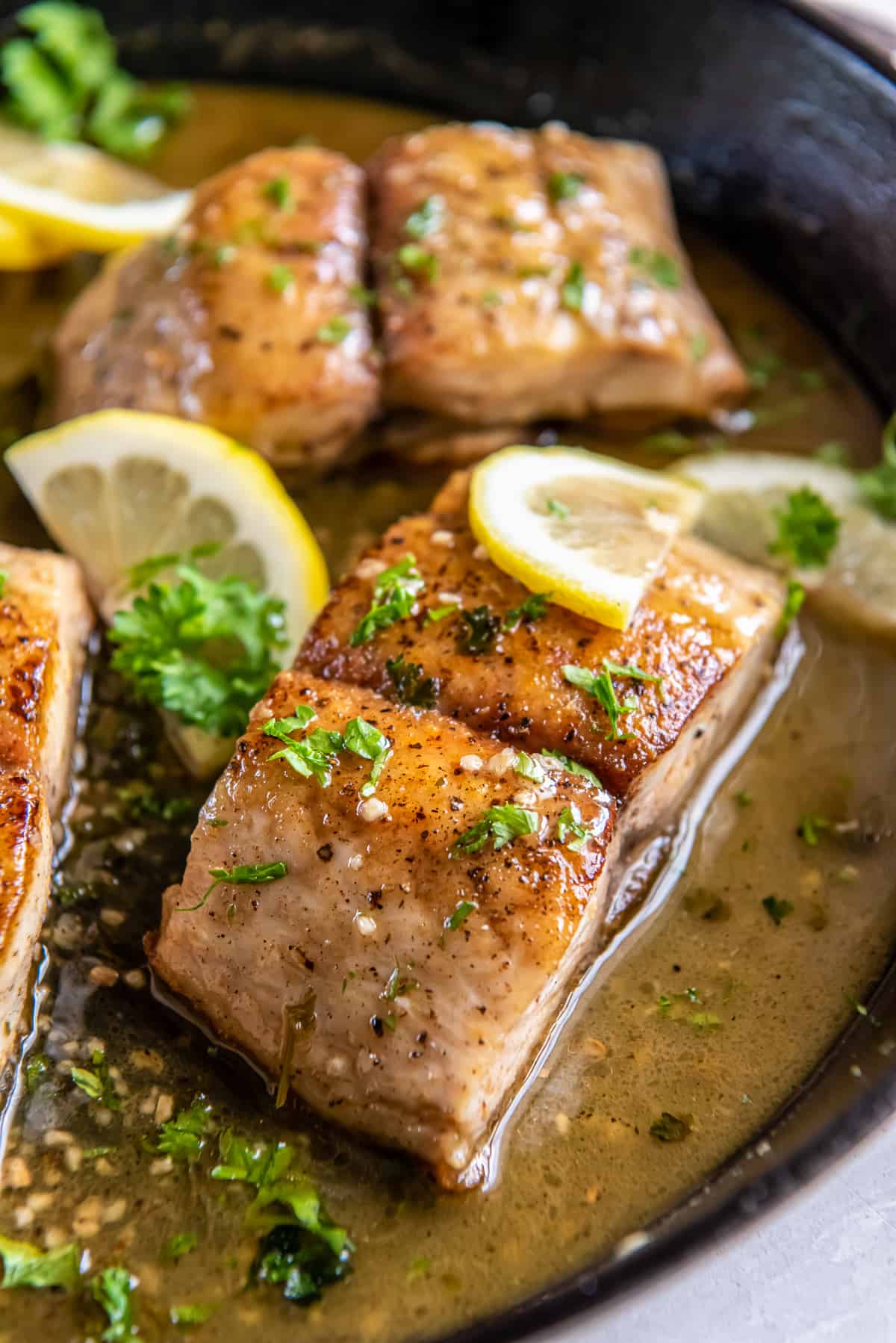 A side view of mahi mahi fillets in a lemon butter sauce in a cast iron skillet.