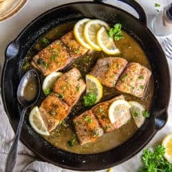 A top down shot of mahi mahi with sauce and lemon in a cast iron skillet with a metal spoon.