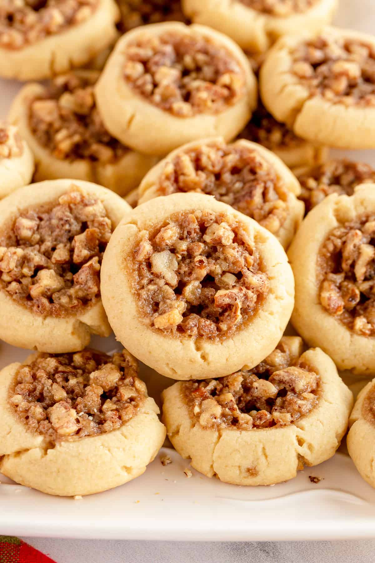 A close up of thumbprint cookies filled with a pecan mixture on a white platter.