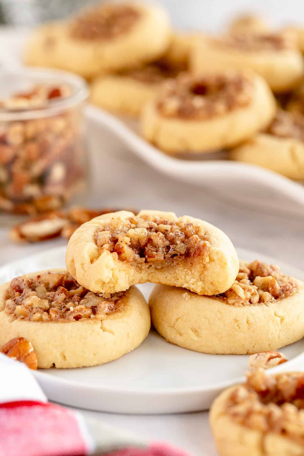 A Pecan Pie Thumbprint Cookie with a bite missing stacked on two cookies on a white plate.