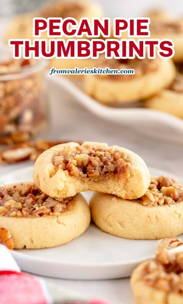 A Pecan Pie Thumbprint Cookie with a bite missing stacked on two cookies on a white plate with text.