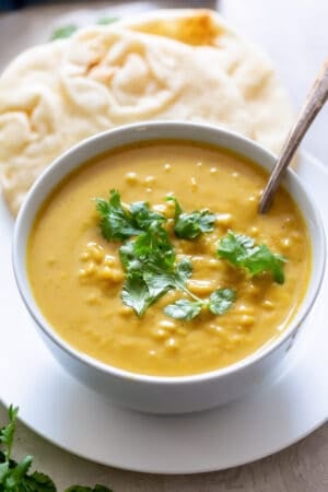 A spoon resting in a white bowl filled with sweet potato curry soup.