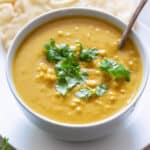 A spoon resting in a white bowl filled with sweet potato curry soup.