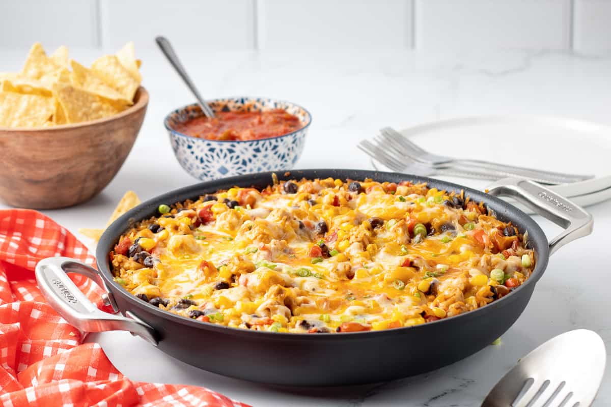 A skillet of tex mex chicken and rice on a white kitchen counter with chips and salsa in the background.