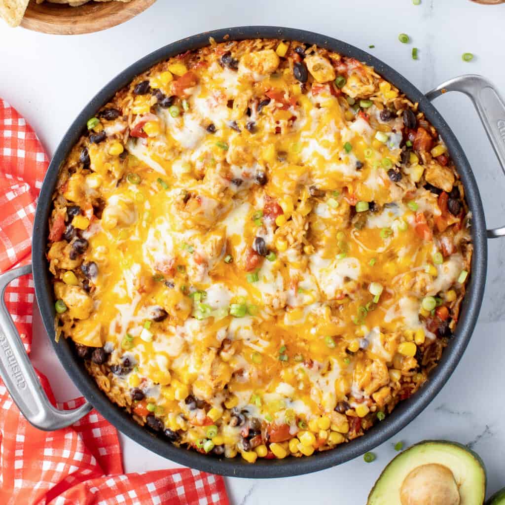 A top down shot of a skillet filled with a chicken and rice mixture with melted cheese.