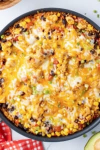 A top down shot of a skillet filled with a chicken and rice mixture with melted cheese.