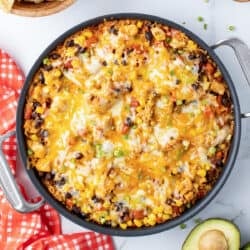 A top down shot of a skillet filled with a chicken and rice mixture with melted cheese.
