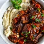 A top down shot a bowl filled with short ribs in a BBQ sauce and mashed potatoes.