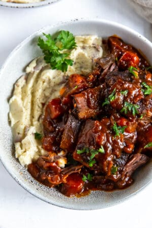 A top down shot a bowl filled with short ribs in a BBQ sauce and mashed potatoes.