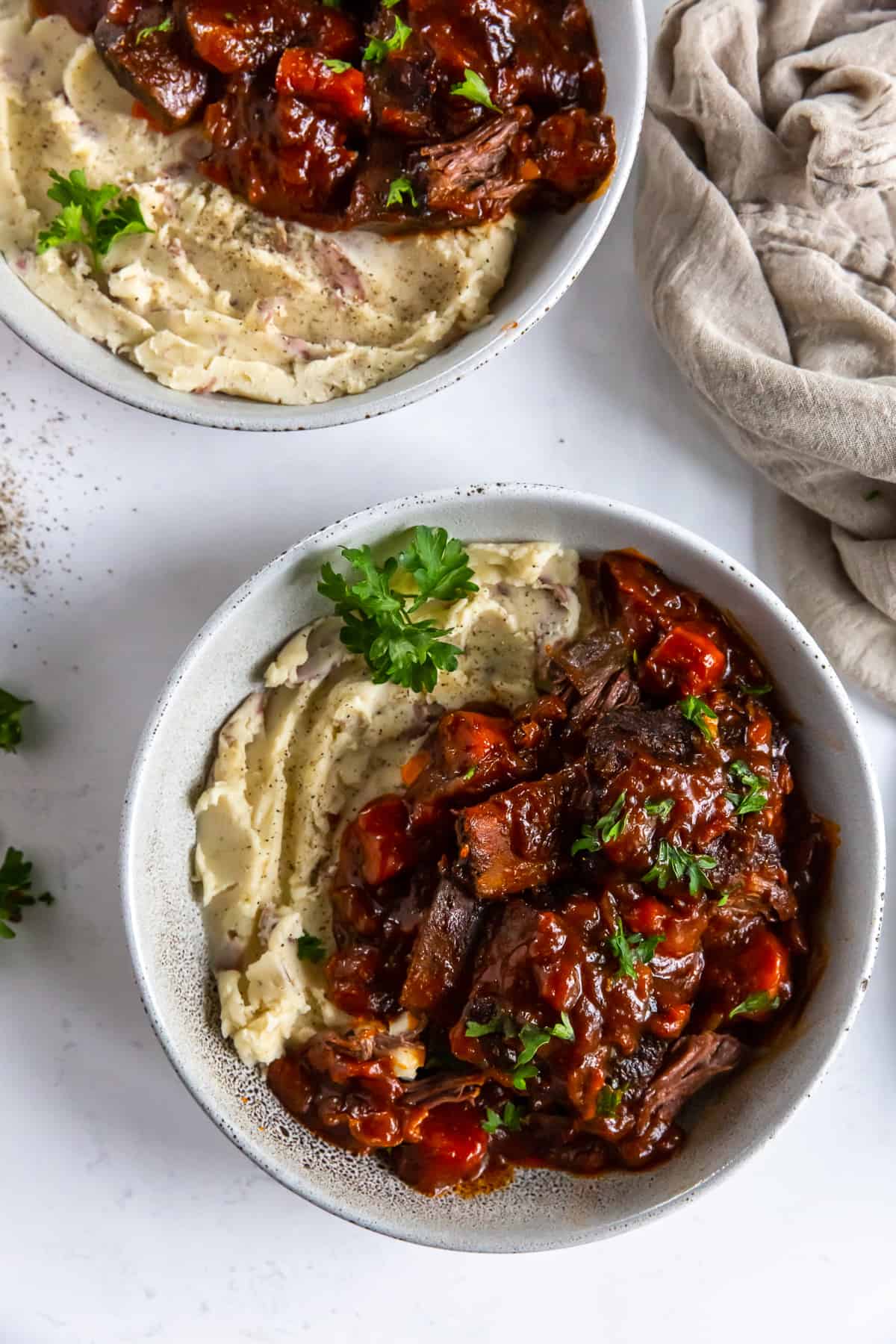 A top down shot of two bowls filled with short ribs in a BBQ sauce and mashed potatoes.