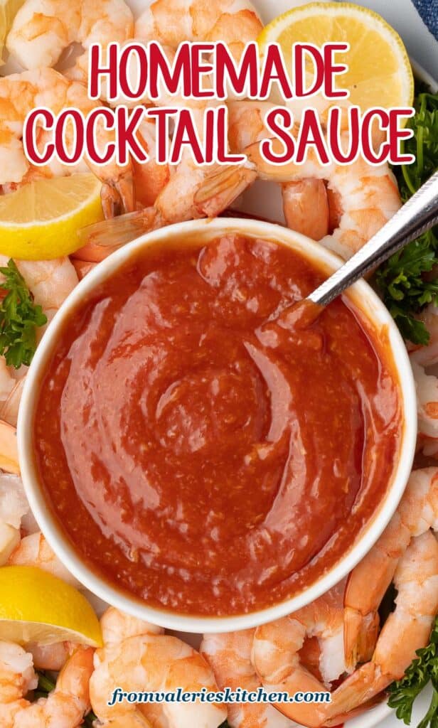 A top down shot of cocktail sauce in a small bowl with a spoon on a platter full of shrimp with text.