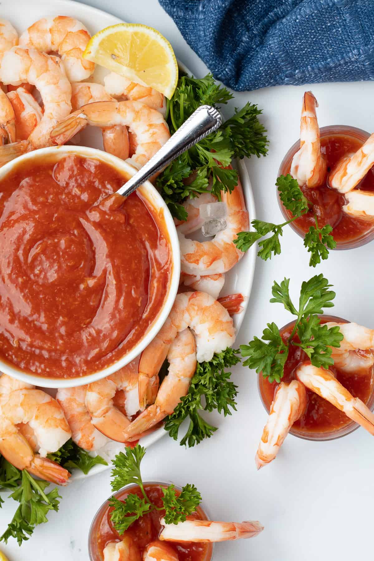 Small cups with cocktail sauce and shrimp next to a platter with more shrimp and a bowl of cocktail sauce.