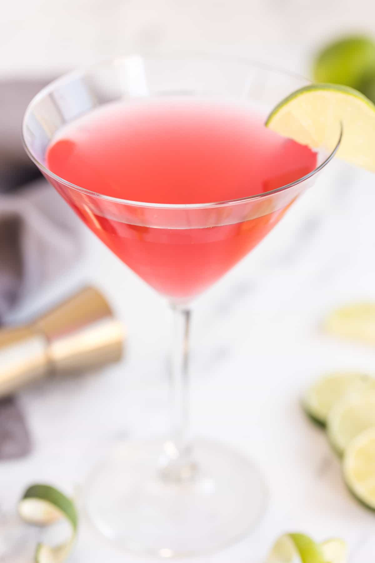 A cosmopolitan cocktail in a martini glass with a slice of lime on the rim on a kitchen counter.