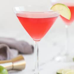 A cosmopolitan cocktail in a martini glass with a slice of lime on the rim on a kitchen counter.
