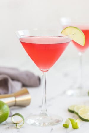 A cosmopolitan cocktail in a martini glass with a slice of lime on the rim on a kitchen counter.