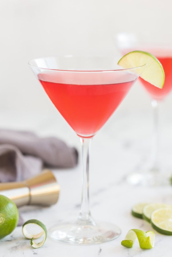 A cosmopolitan cocktail in a martini glass with a slice of lime on the rim on a kitchen counter.