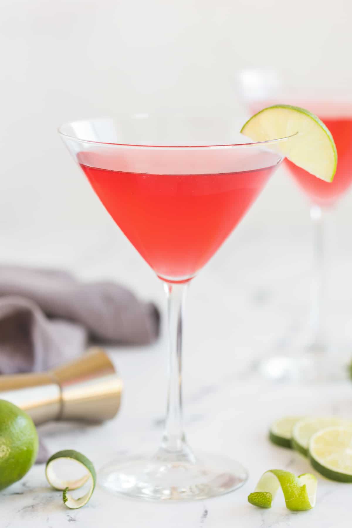 A cosmopolitan cocktail in a martini glass  with a slice of lime on the rim on a kitchen counter.