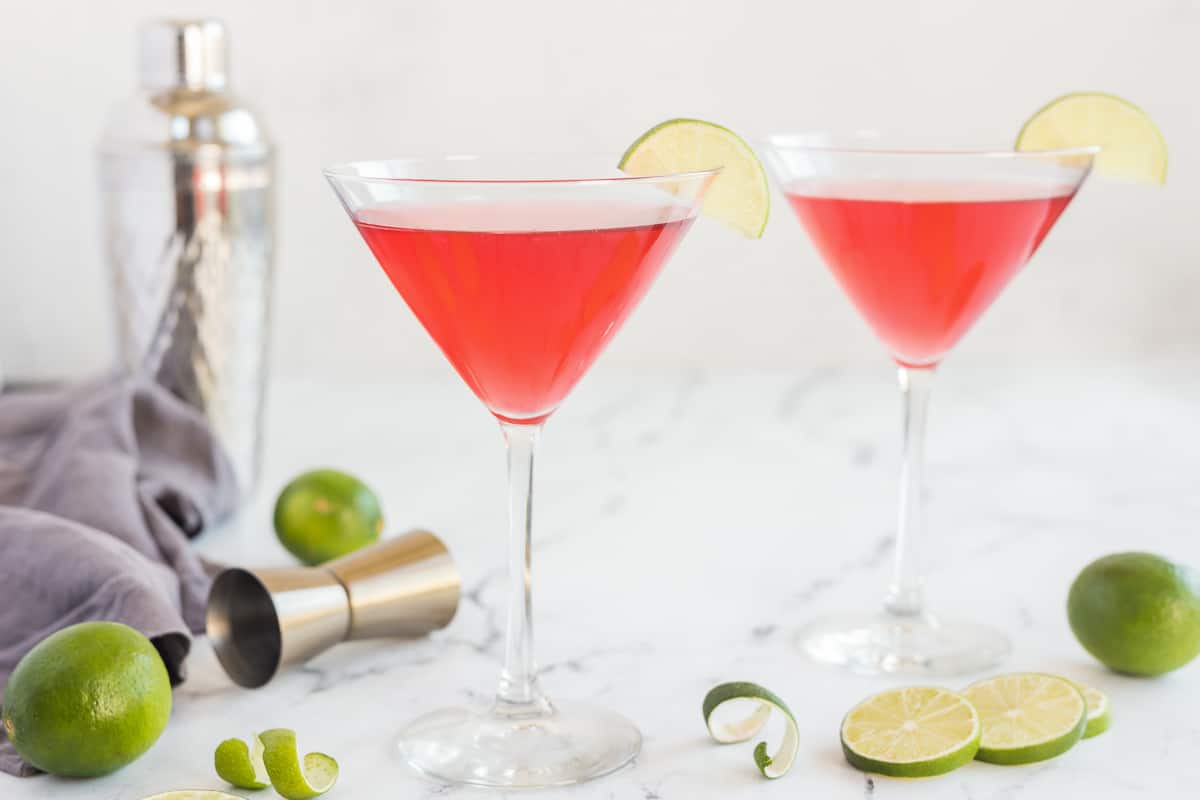 Two cosmopolitan cocktails in martini glasses with a lime slice on the rims.