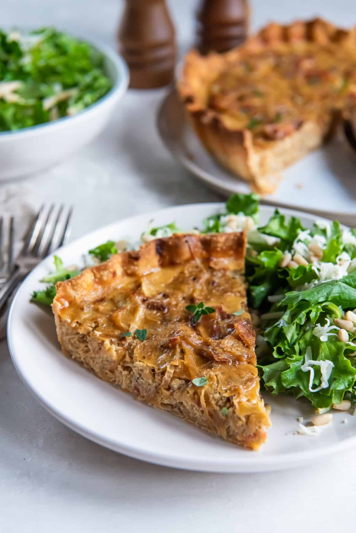 A plate with a slice of onion tart and green salad on a table.