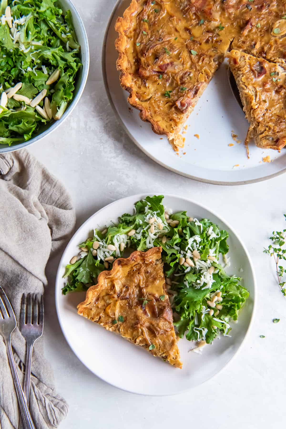 A plate with a slice of onion tart and green salad on a table.