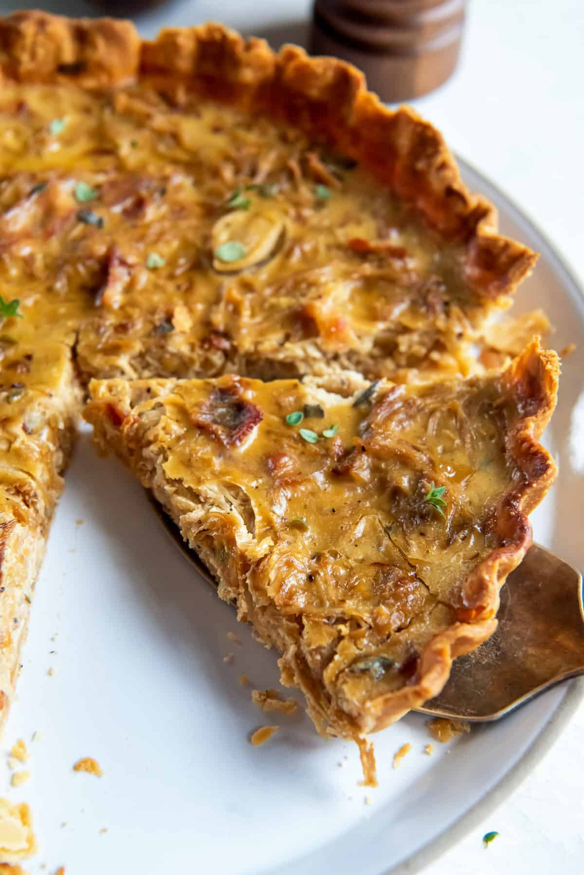 A spatula lifting a slice of onion tart from a platter.