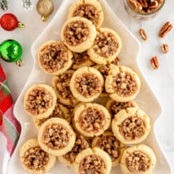 Pecan Pie Thumbprint Cookies on a Christmas tree shaped platter surrounded by ornaments.