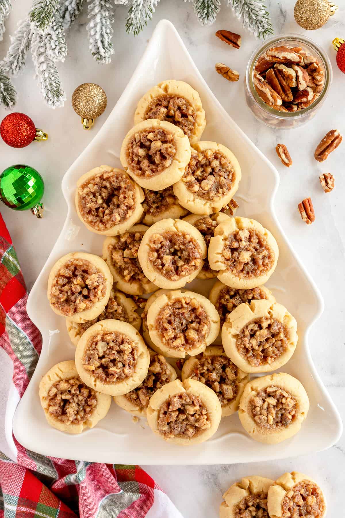 Pecan Pie Thumbprint Cookies on a Christmas tree shaped platter surrounded by ornaments.