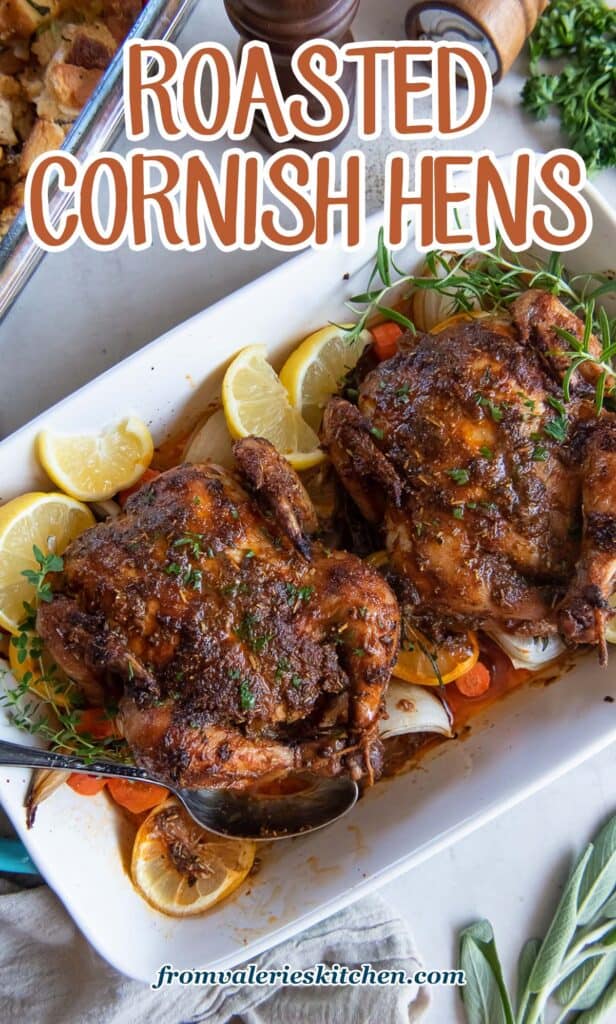 A top down shot of two roasted cornish game hens in a baking dish with a spoon with text.