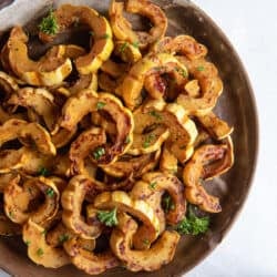 A top down shot of roasted delicata squash on a round wooden platter.