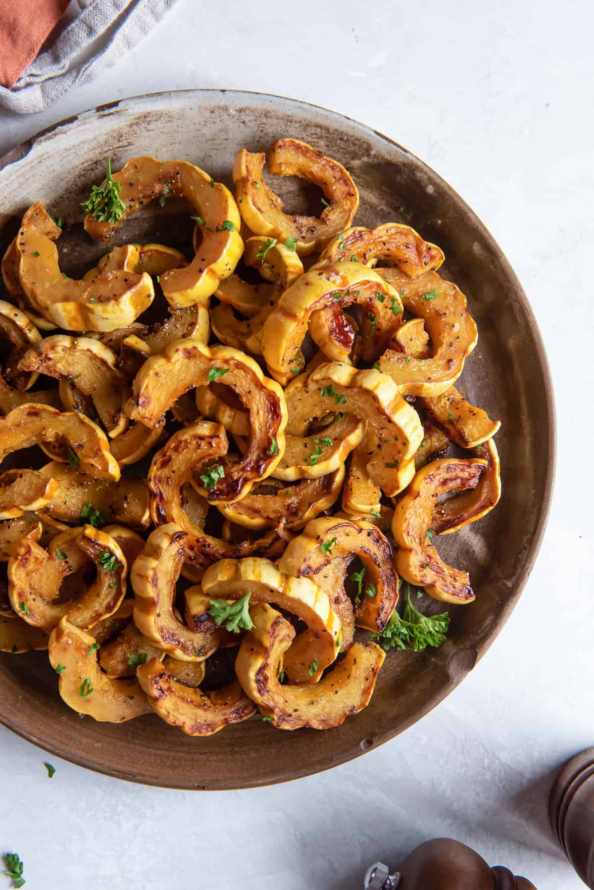 A top down shot of roasted delicata squash on a round wooden platter.