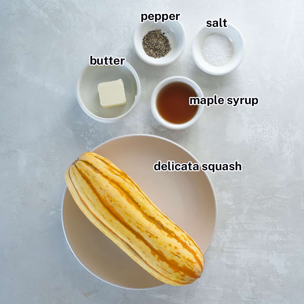 A delicata squash on a plate next to small bowls filled with butter, maple syrup, salt and pepper with text.