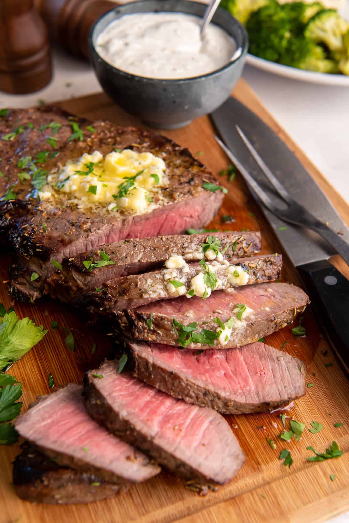 Sliced London Broil topped with melting blue cheese butter on a wood board.