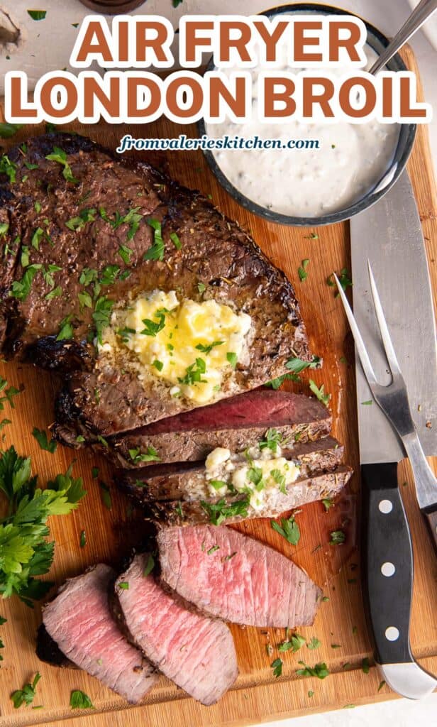 A top down shot of a partially sliced London Broil topped with melting blue cheese butter on a wood board with a small bowl of a creamy sauce with text.