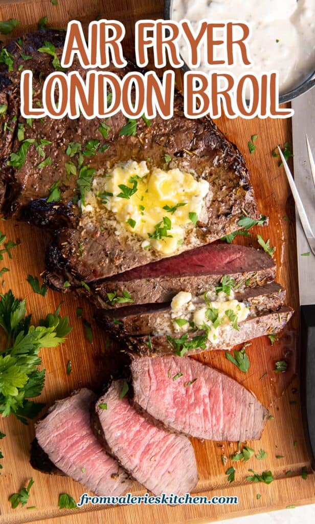 A top down shot of a partially sliced London Broil topped with melting blue cheese butter on a wood board with a small bowl of a creamy sauce with text.