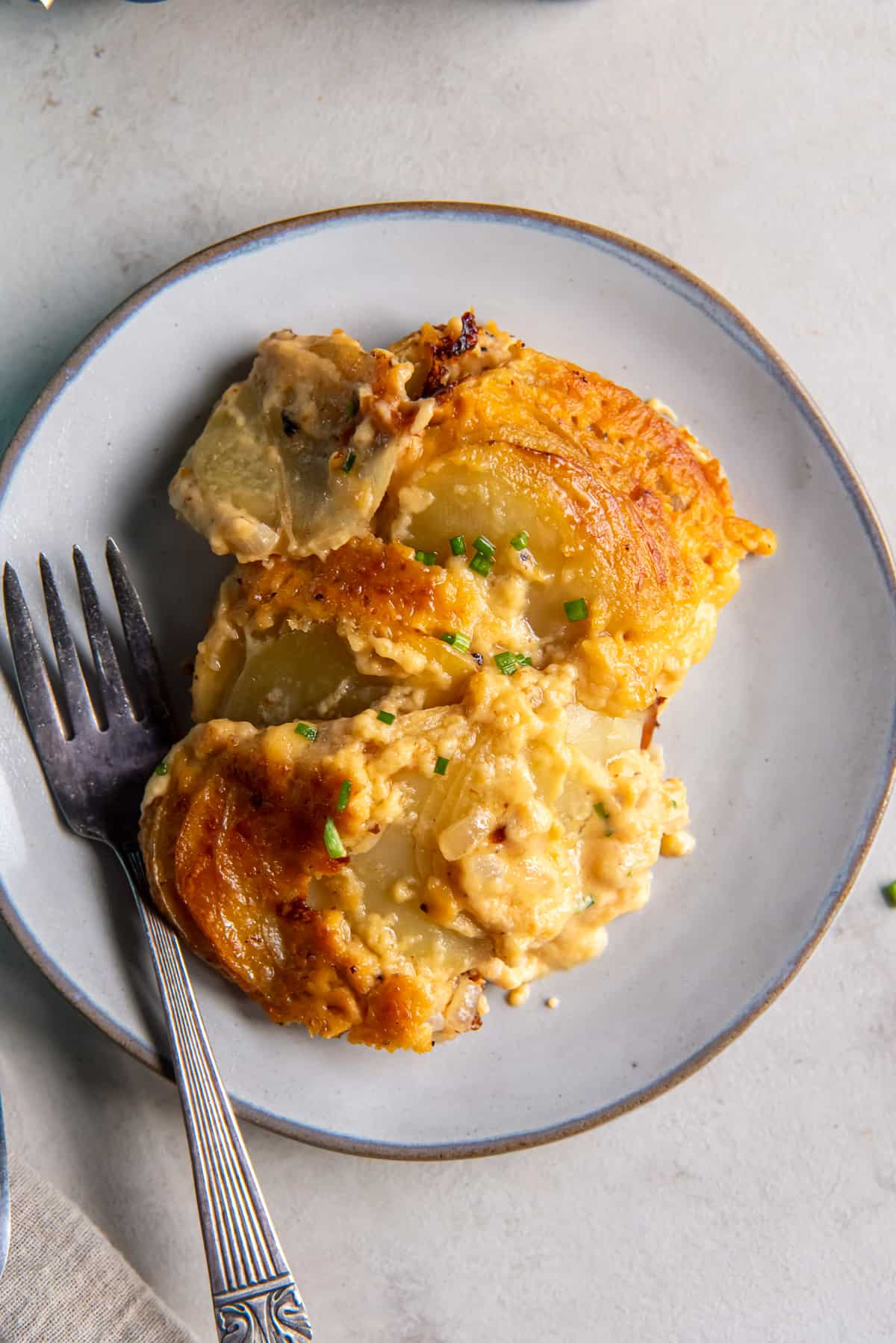 A serving of cheesy au gratin potatoes on a white plate with a fork.