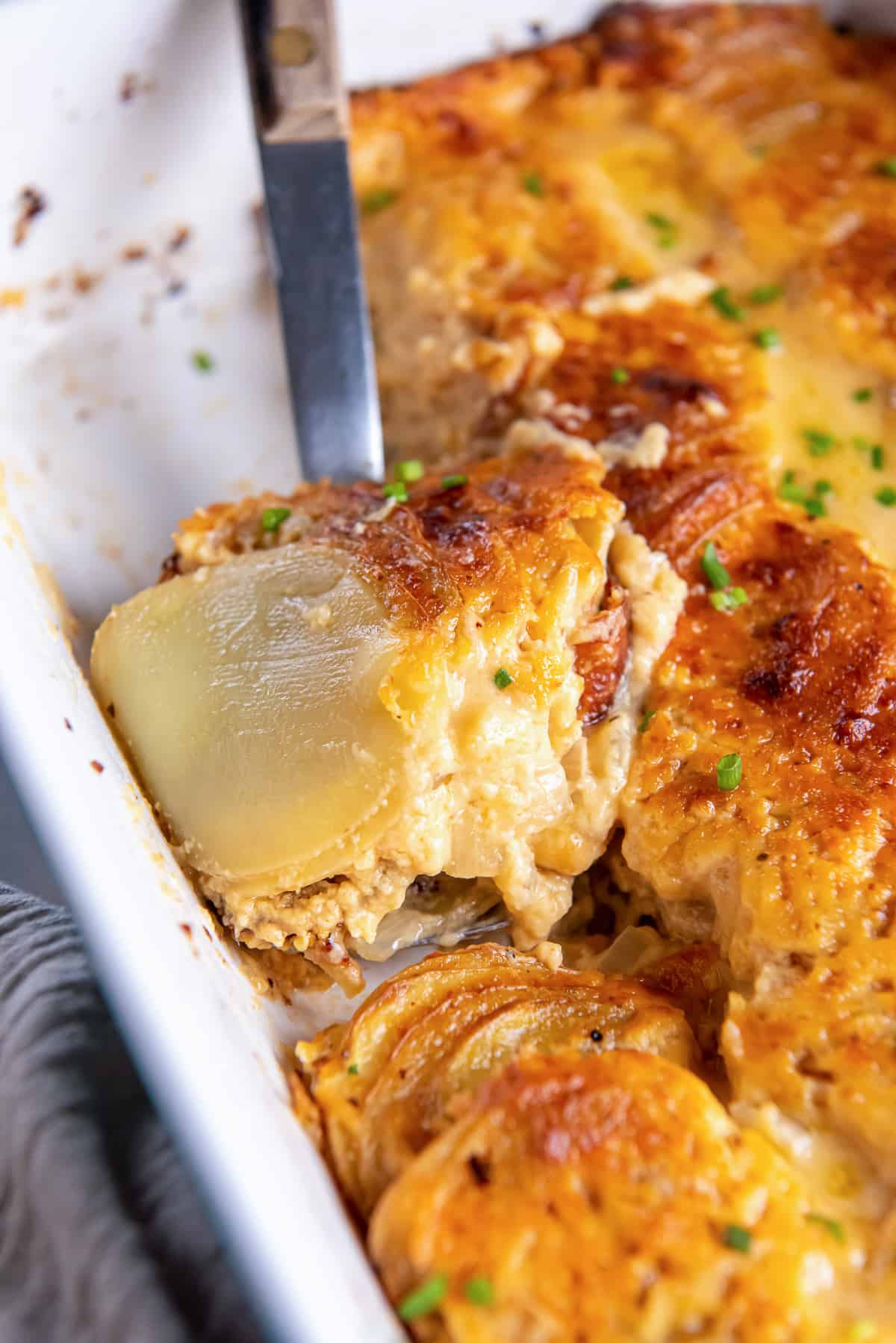 A spoon scoops au gratin potatoes from a baking dish.