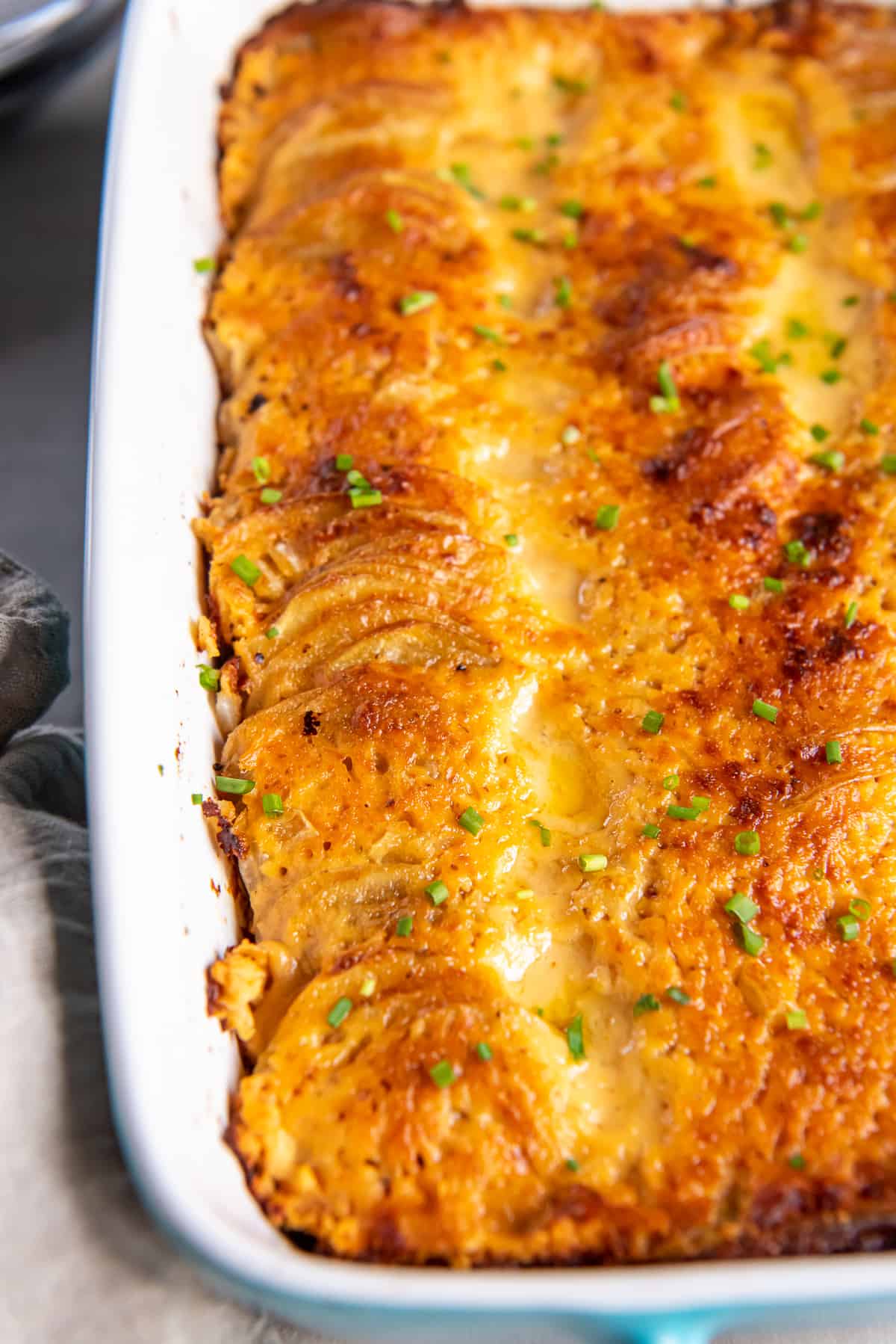 A close up top down shot of au gratin potatoes with a golden, cheesy top in a white baking dish.