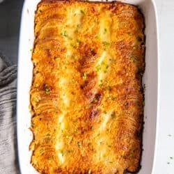 A top down shot of au gratin potatoes in a baking dish with blue handles next to a grey cloth.