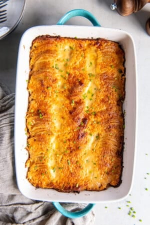 A top down shot of au gratin potatoes in a baking dish with blue handles next to a grey cloth.