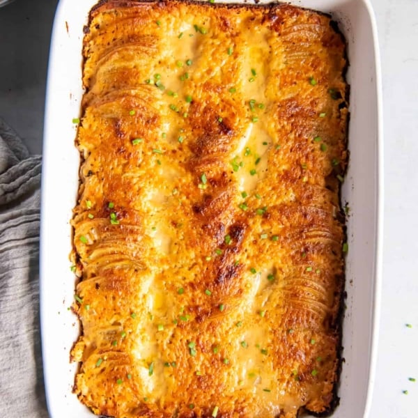 A top down shot of au gratin potatoes in a baking dish with blue handles next to a grey cloth.