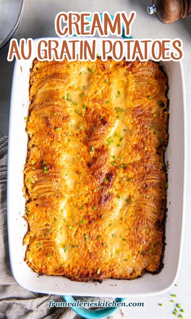 A top down shot of au gratin potatoes in a baking dish with blue handles next to a grey cloth with text.