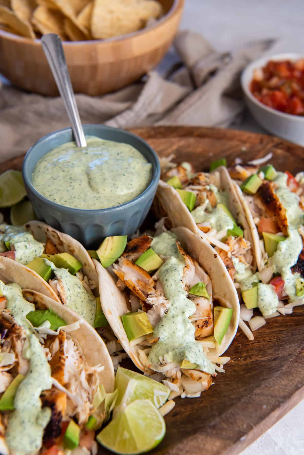 Fish tacos with cabbage and avocados on a wood board with a small bowl of cilantro lime sauce behind them.