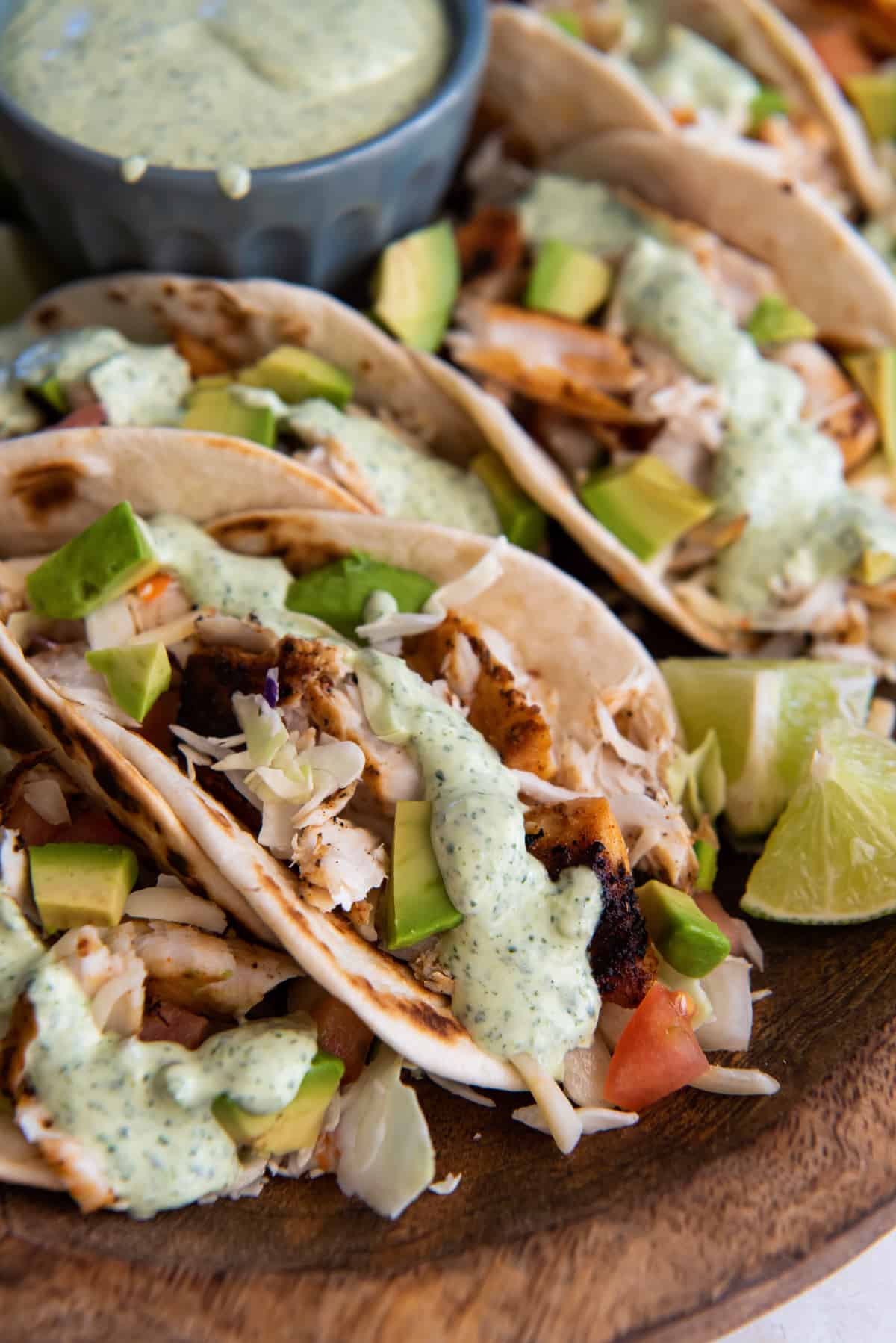 A close up of fish tacos with cabbage, avocados, and cilantro lime sauce on a wood board.