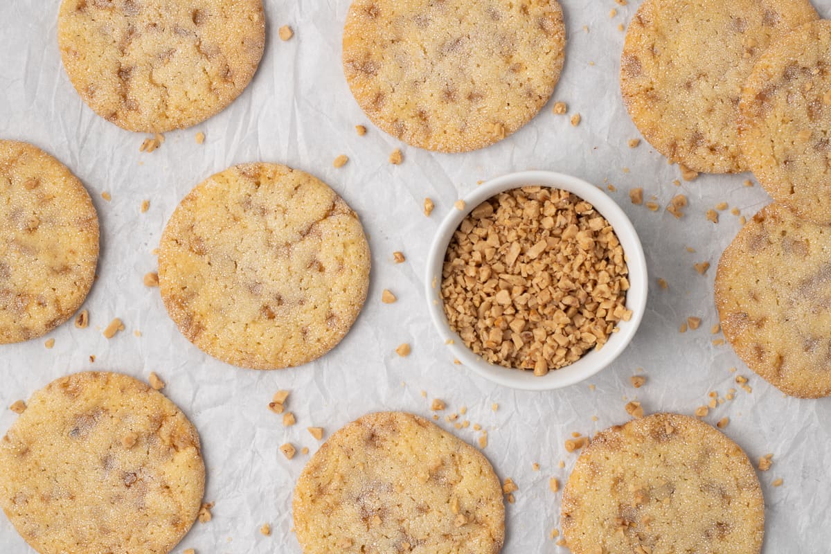 A top down shot of cookies on parchment paper next to a small bowl of toffee bits.